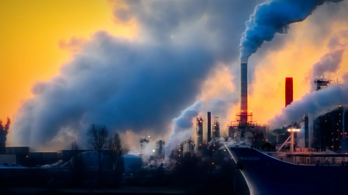 An image showing a boat in the sea with a background of industrial buildnings and their emissions in the air.