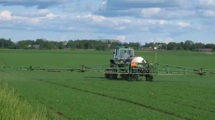 Traktor med bekämpningsmedelsspruta på ett fält