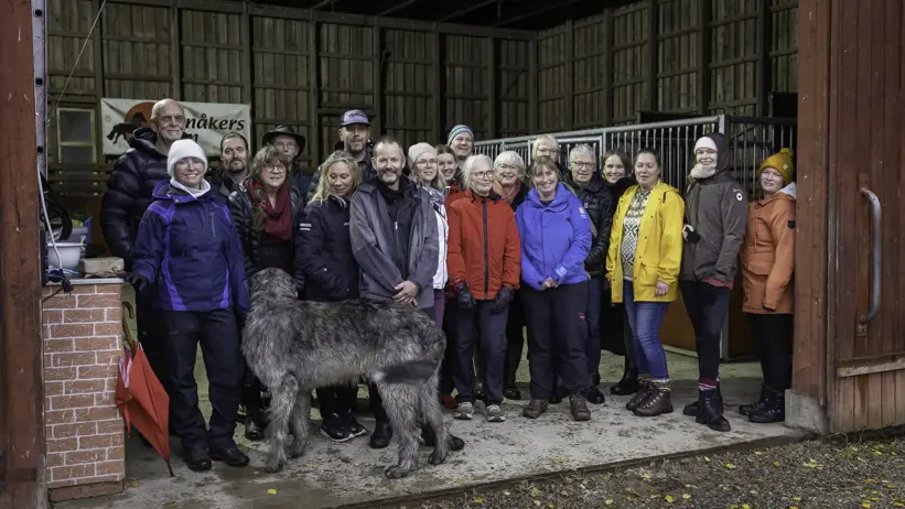 Participants in a workshop standing in stables with raincoats