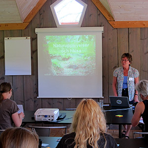 Bild på en kvinna som står framför en publik. Hon håller en presentation.