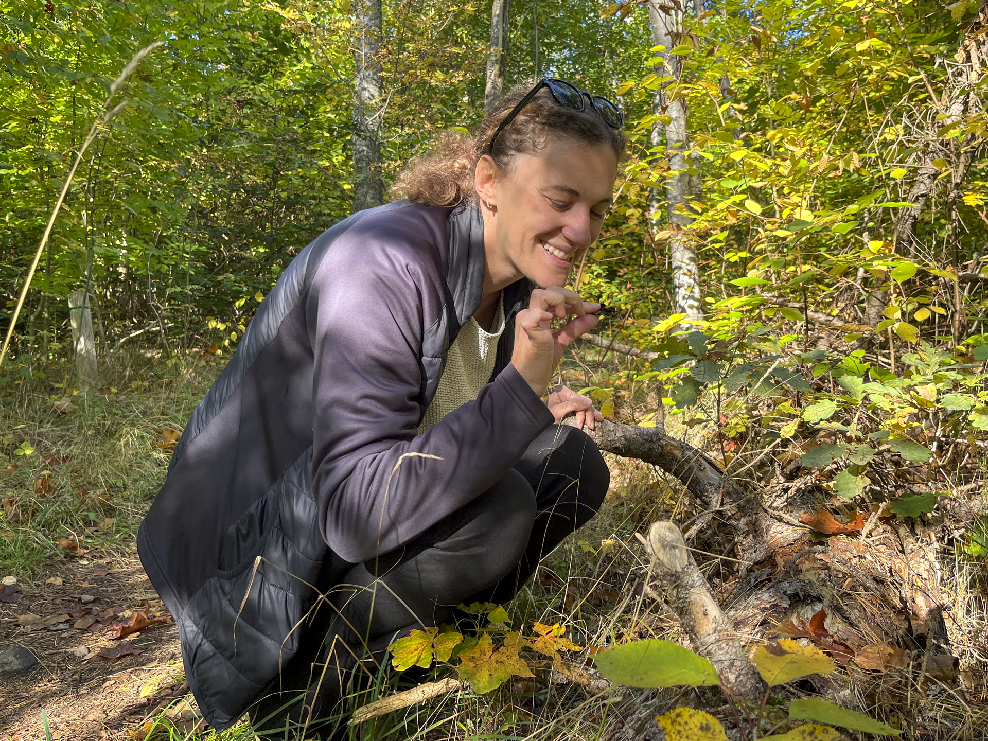 Francesca sits by a fallen tree and picks up a bit of moss.