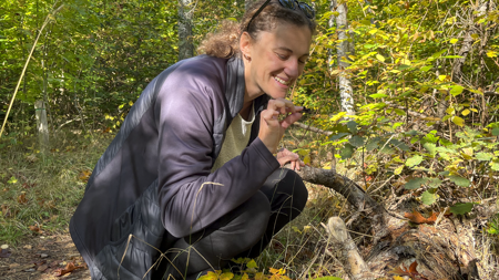 Francesca sits by a fallen tree and picks up a bit of moss.
