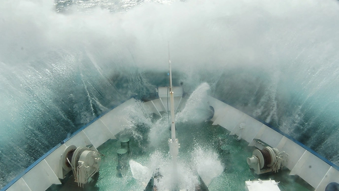 Large waves crash over the bow of a ship at sea during heavy weather.