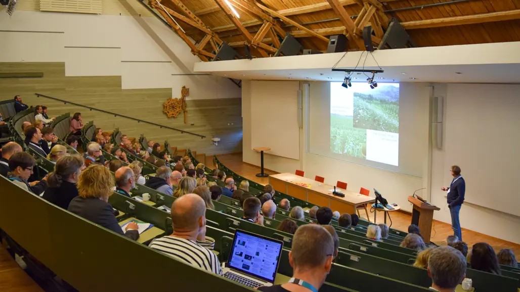 En hörsal full med folk, en presentatör vid podiet. Foto.
