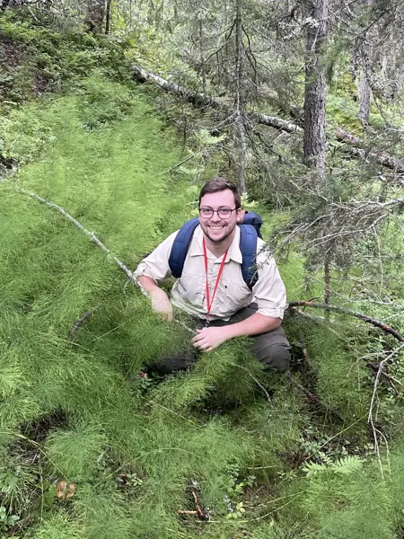 A man is crouching in the woods.