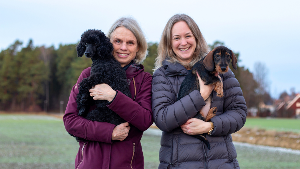 Två kvinnor som står bredvid varandra, med varsin hund i sin famn.