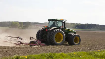 En traktor med harv kör på ett fält.