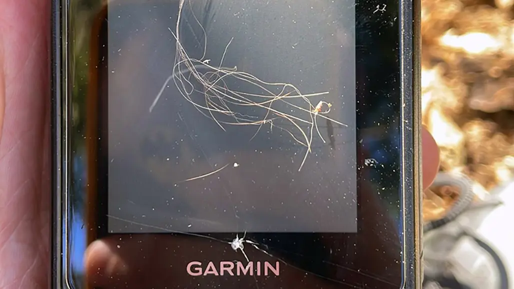 Närbild av en Garmin-enhet med långa hårstrån, som ligger på skärmen. Texten "GARMIN" är synlig längst ner. Foto.