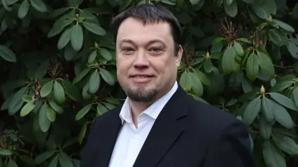 Person utomhus framför gröna blad.