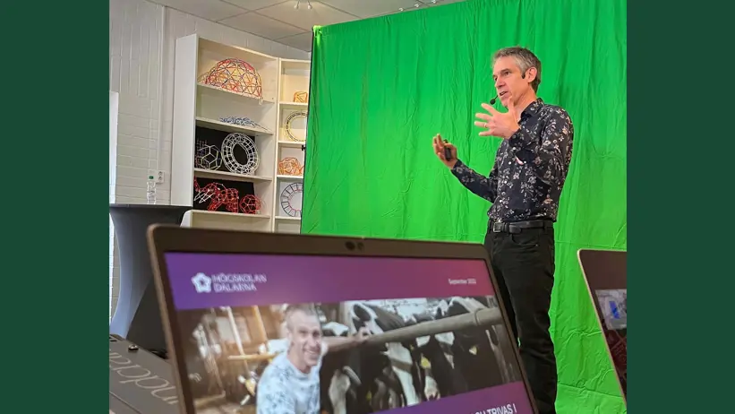 Photo of a man giving a lecture standing in front of a green screen.