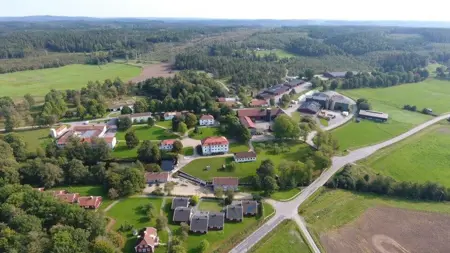 Flygbild över Strömma Naturbrukscentrum, byggnader, skogspartier och åkrar.