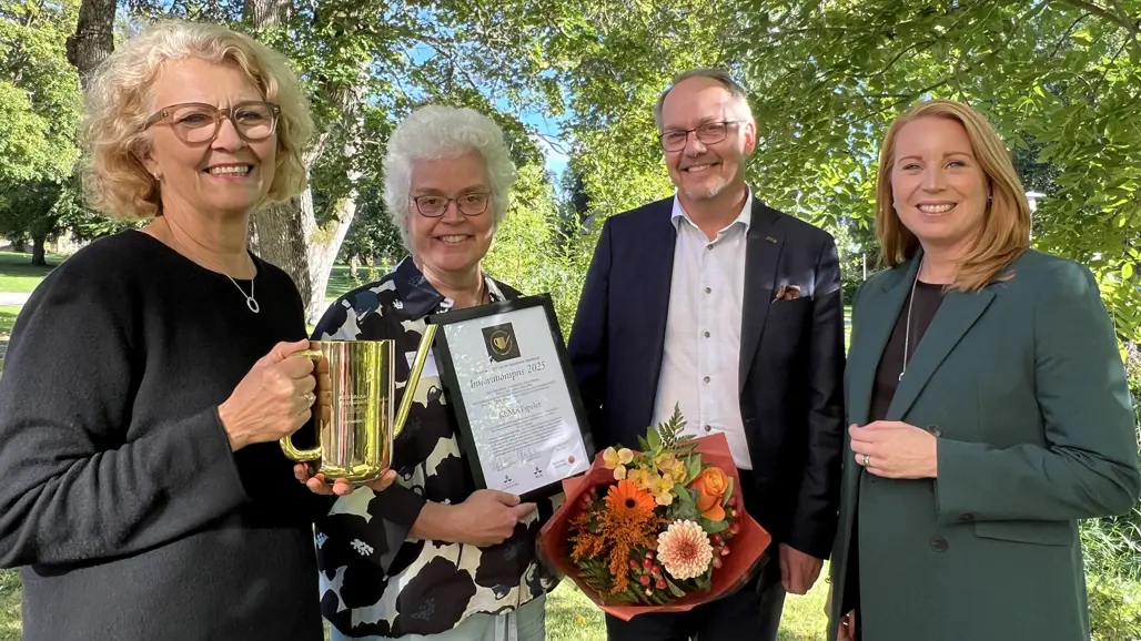 Fyra personer med blommor och pris står utomhus i grön omgivning