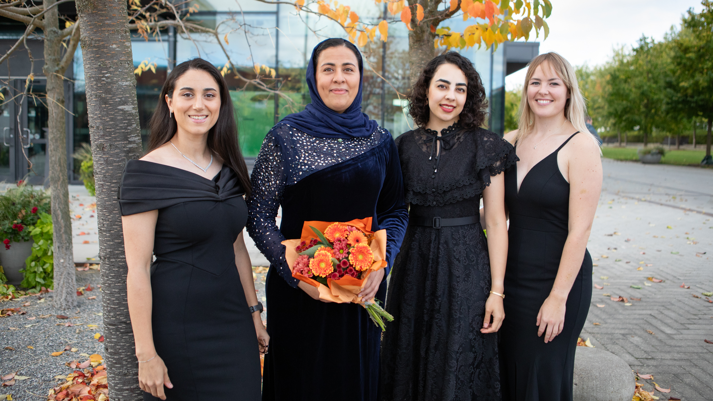 Four persons in dark festive dresses standing outside smiling into the camera.