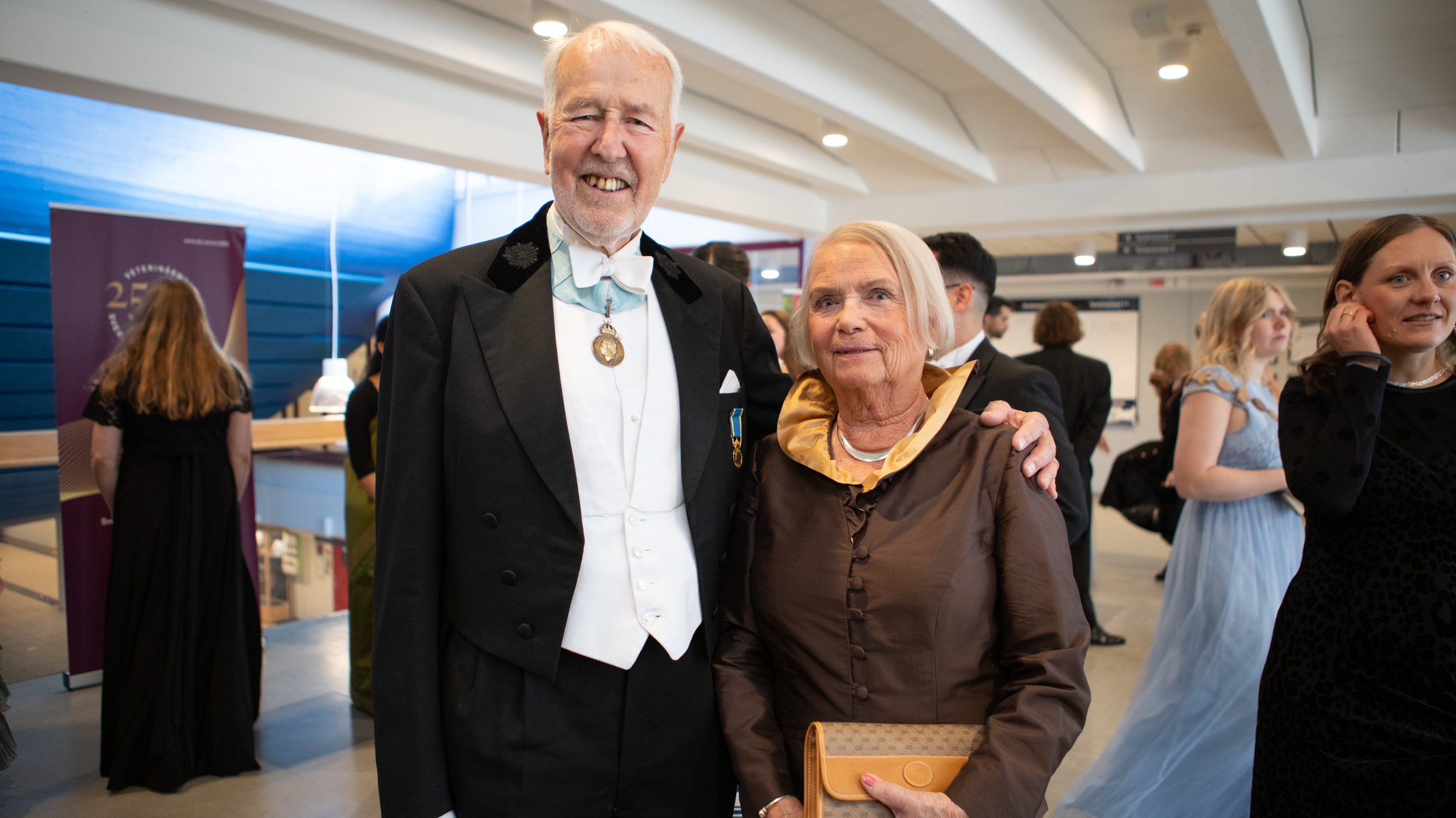Two elderly persons wearing festive dresses smiling into the camera. One of them wearing a medal.