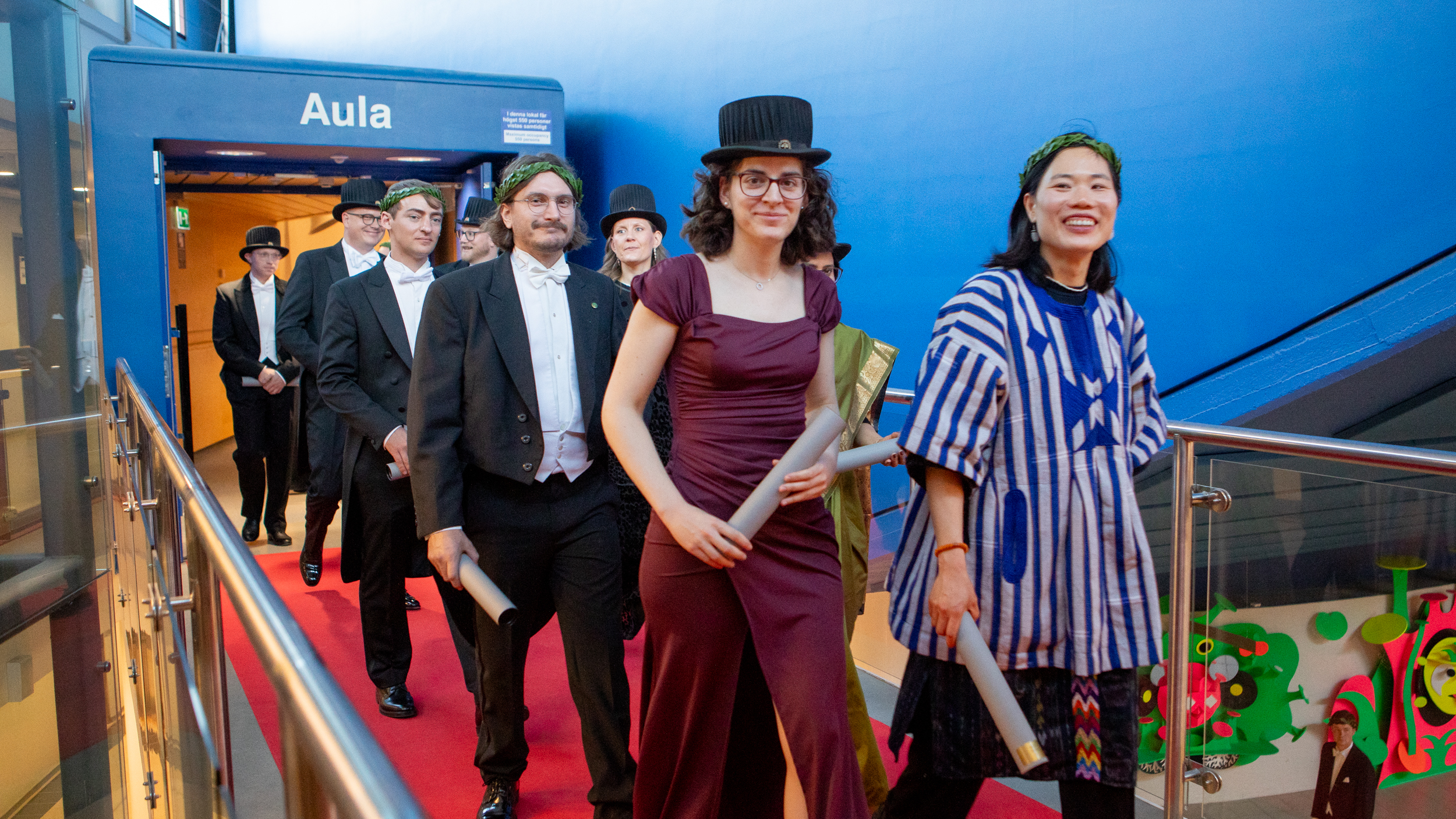 Happy festively dressed people wearing doctoral hats and laurel wreaths walking in procession.