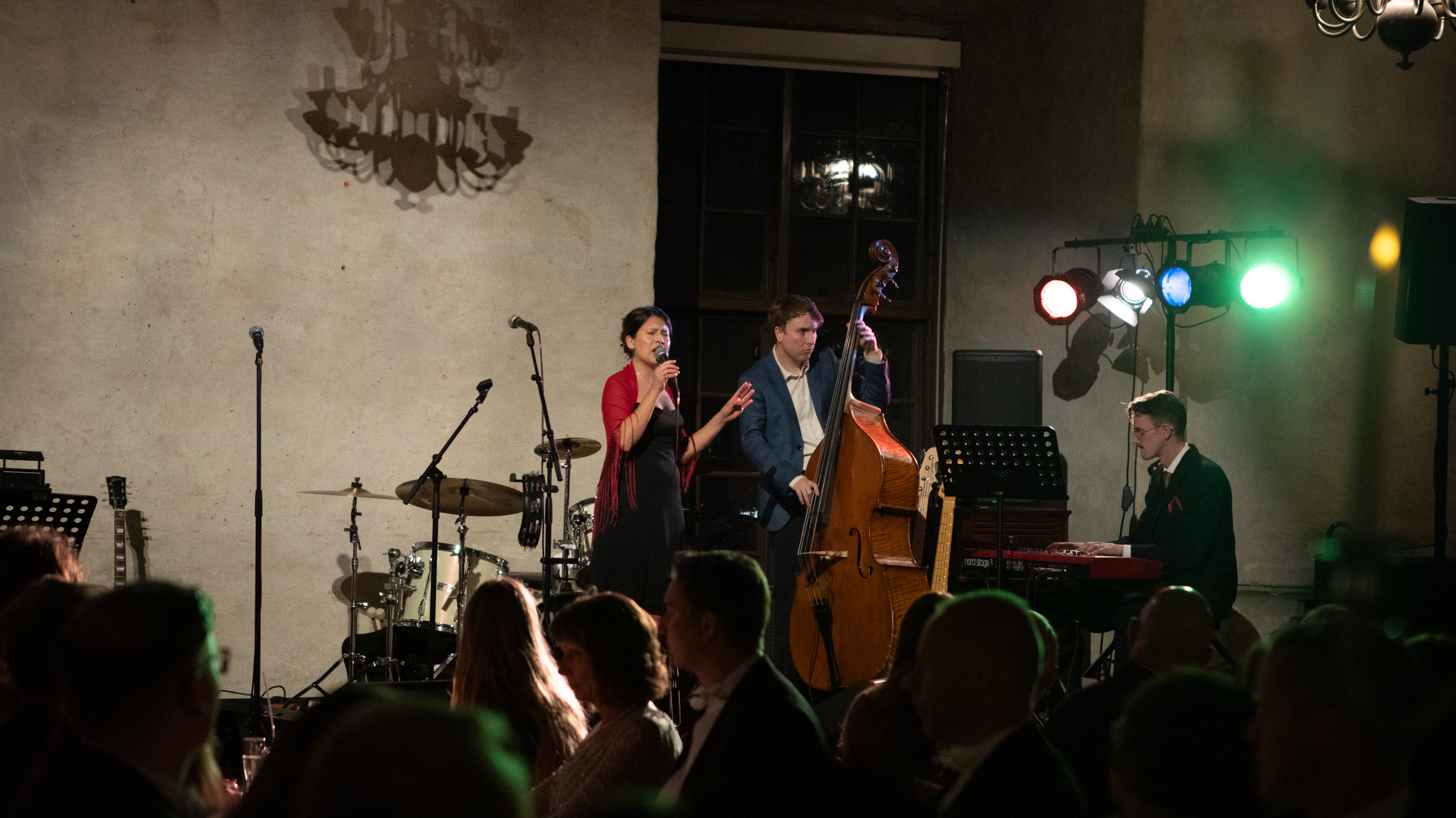 A singer, a bass player and a keyboardist on a stage in a large hall.