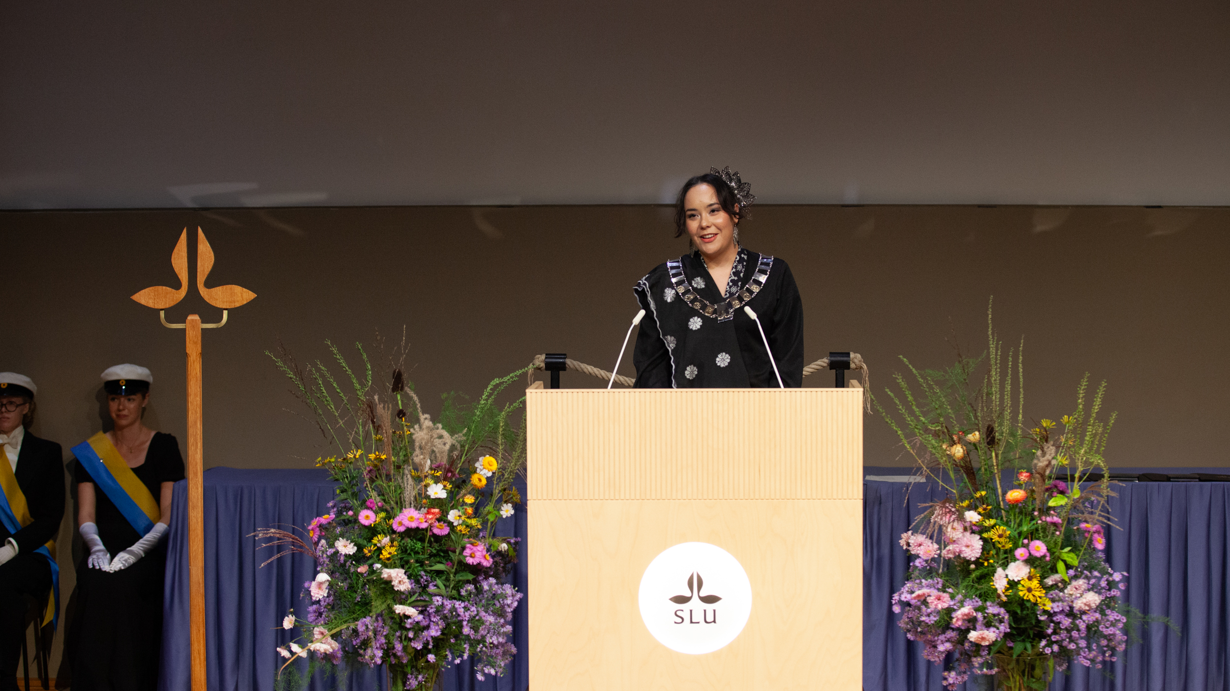 A young festively dressed person standing at a lectern on a stage.