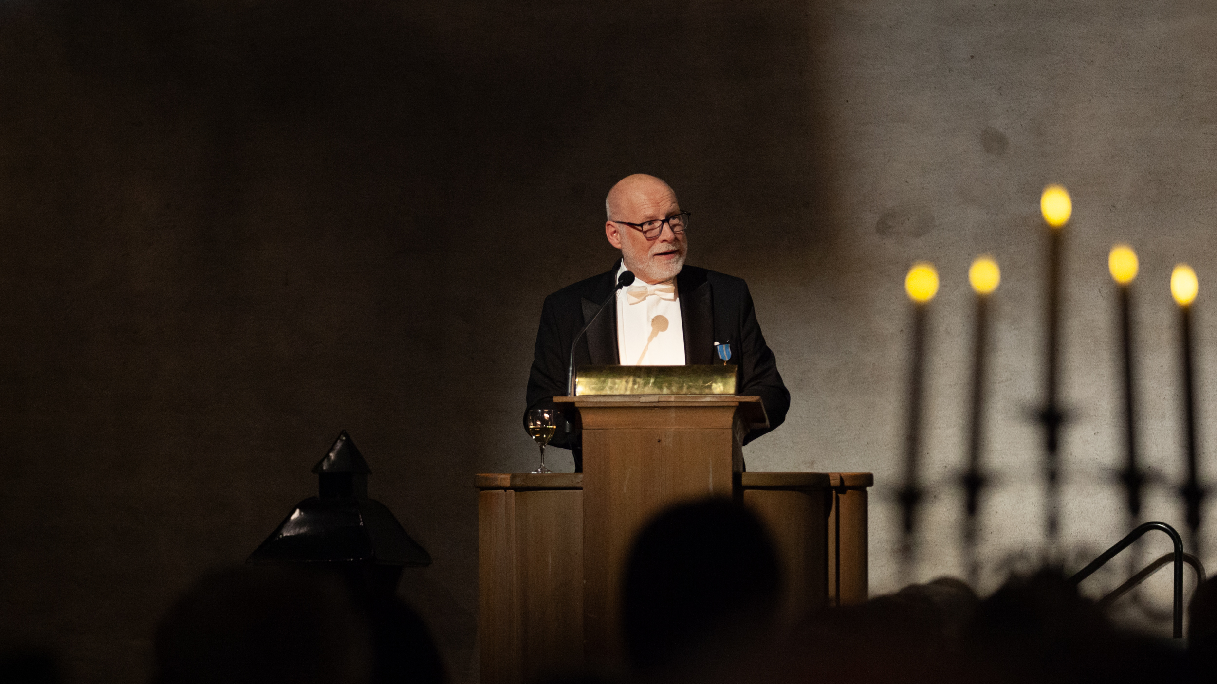 A man dressed in white tie standing at a lectern in a big hall. 