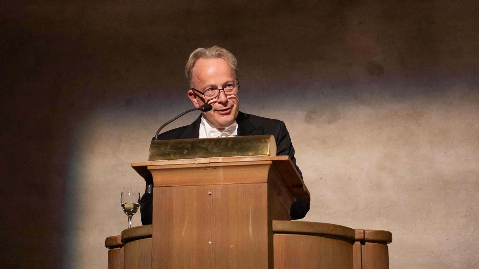 En person i frack och glasögon står i en talarstol.