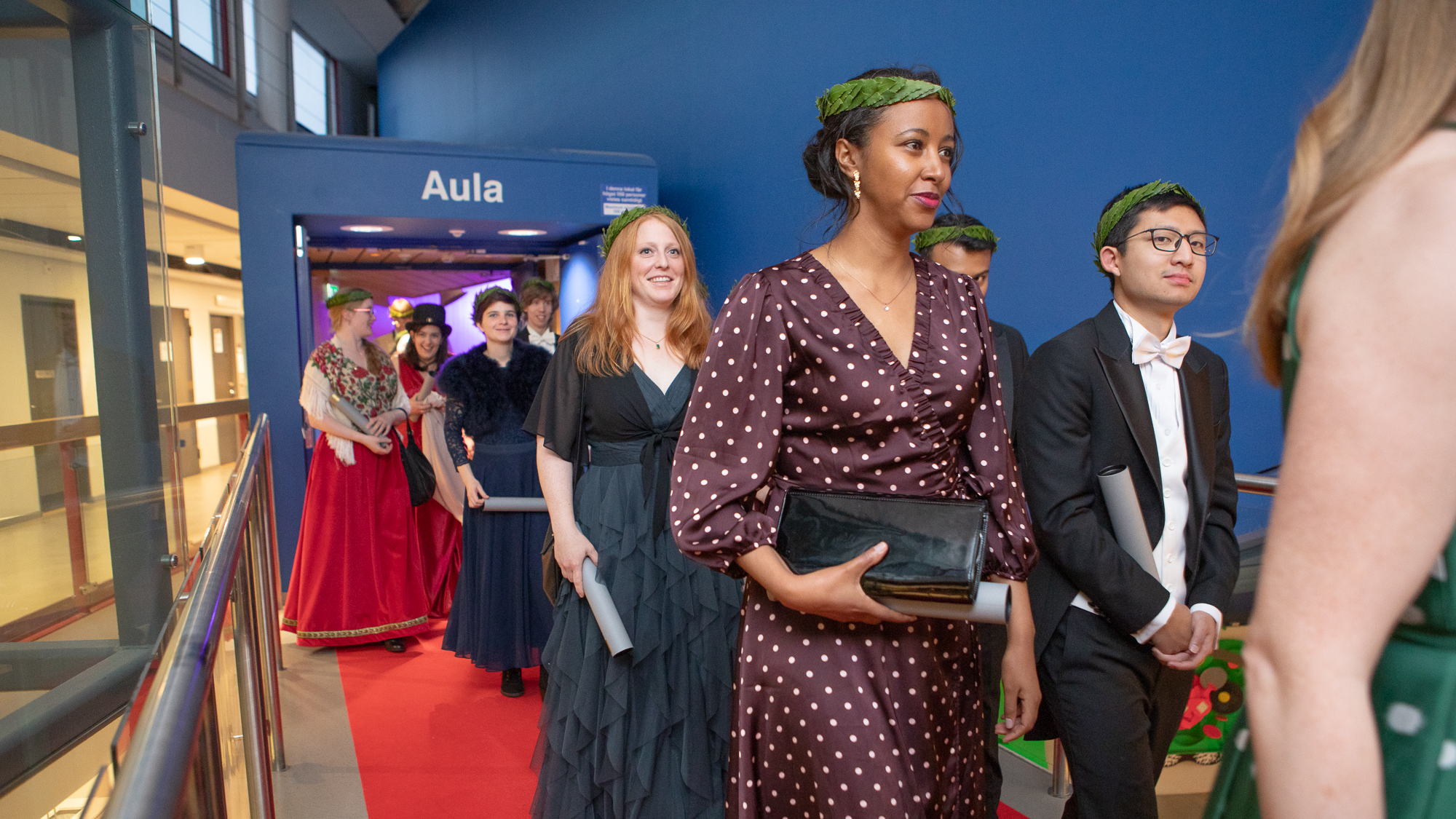 Glada festklädda personer går på led iförda doktorshattar och lagerkransar.