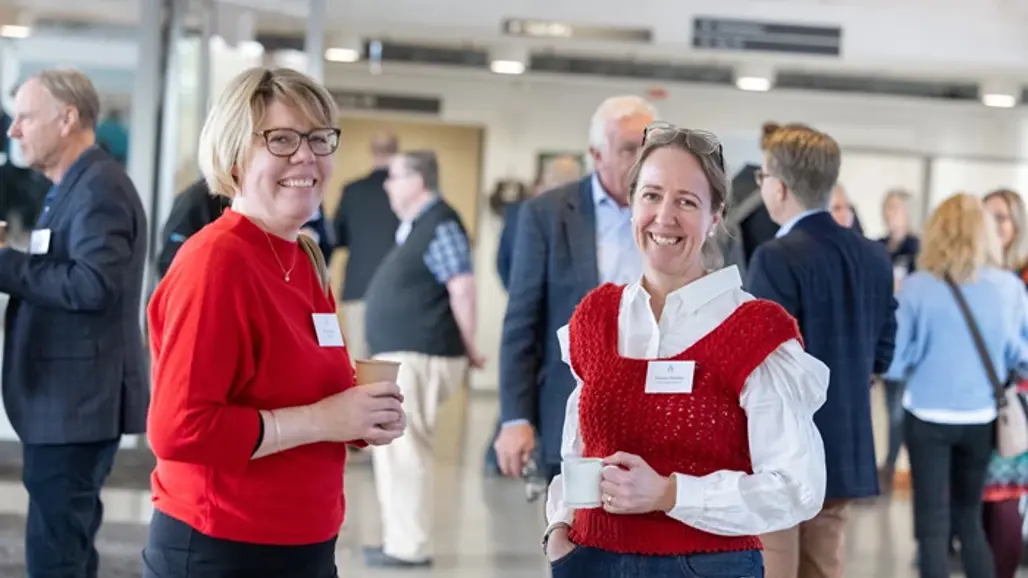 Två kvinnor i röda tröjor i en folksamling inomhus