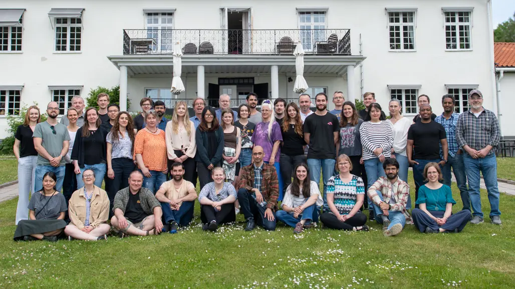 Gruppfoto av många personer utanför en vit byggnad.