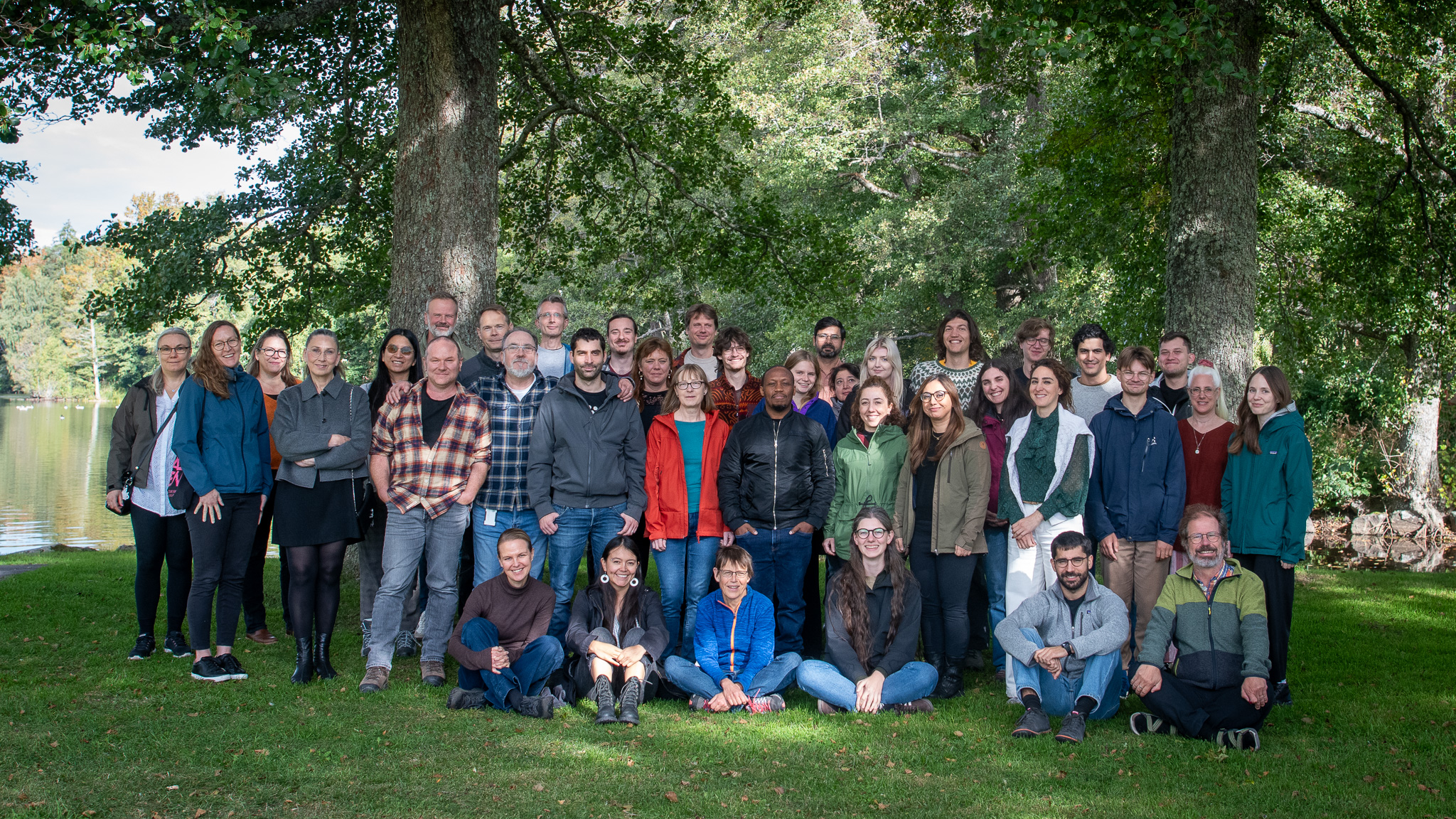 A group photo outdoors with a lake in the background. Photo.