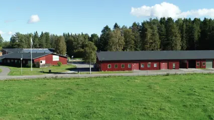 Två röda byggnader längs en väg och skog i bakgrunden.