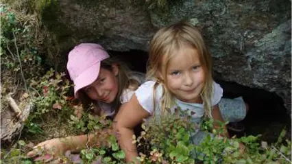 Två barn som leker i skogen bland stenblock.
