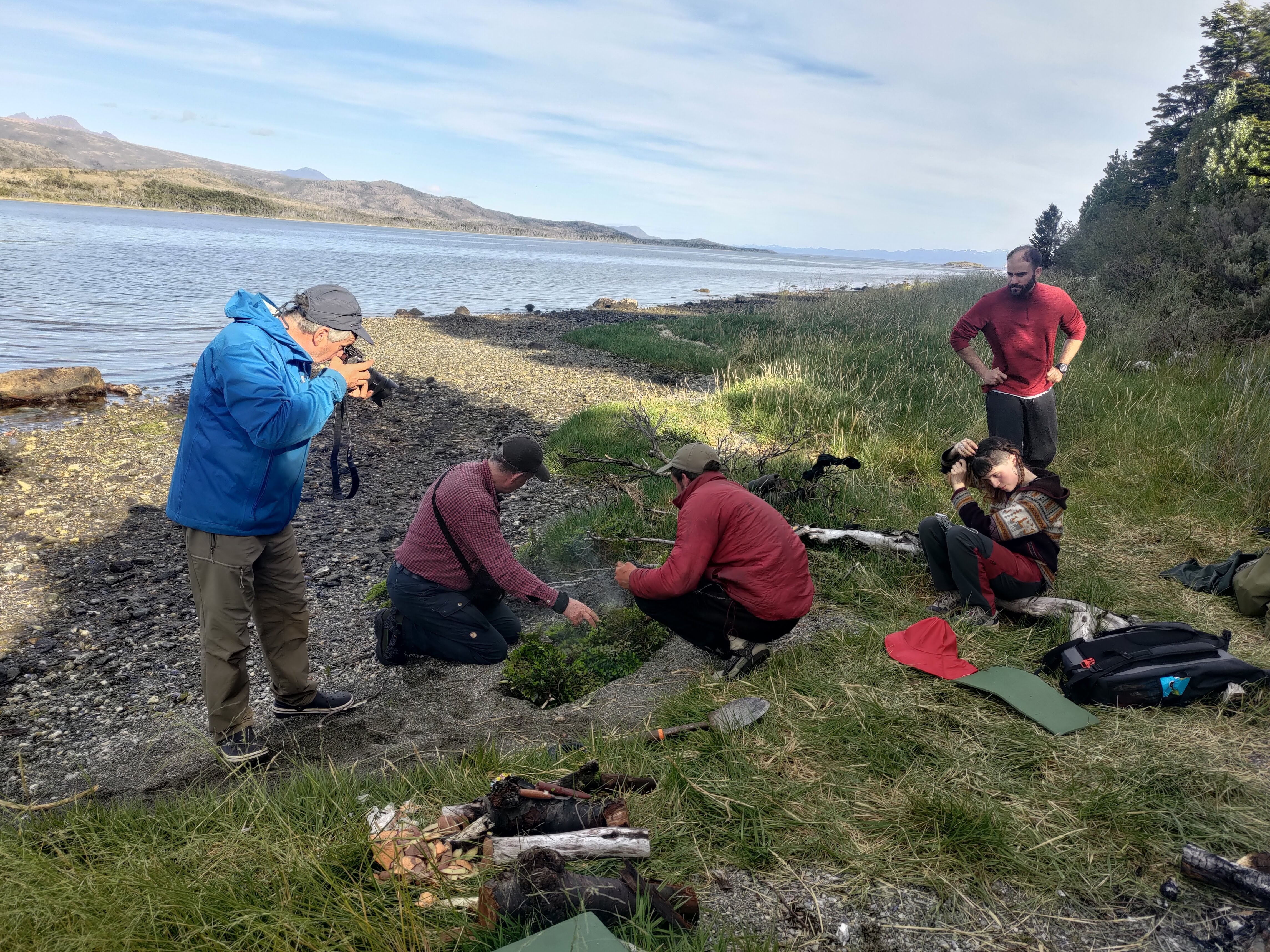 Fieldwork on a shoreline where several people examine the ground and document findings.
