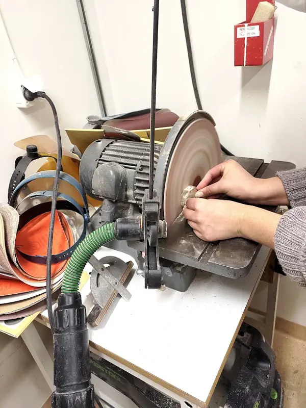 Händer slipar en träbit på en bandslip.