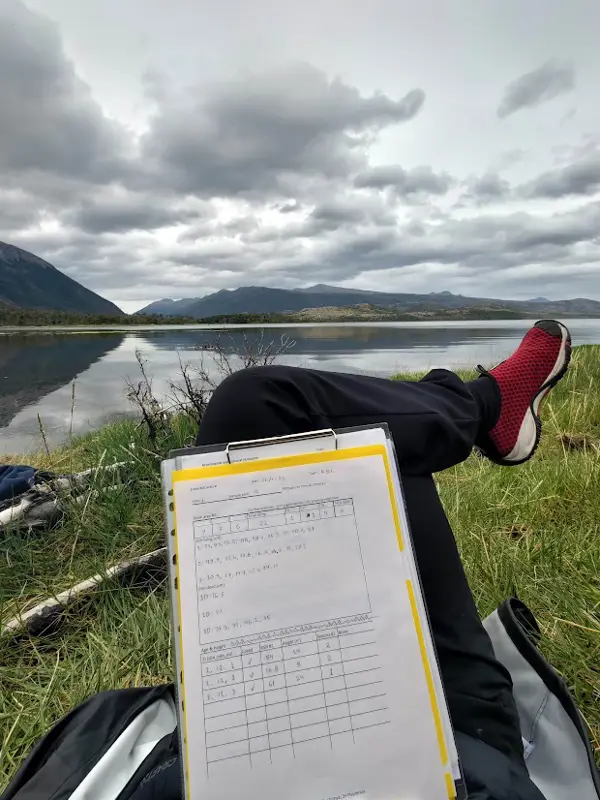 Anteckningar studeras vid en sjö med berg i bakgrunden.