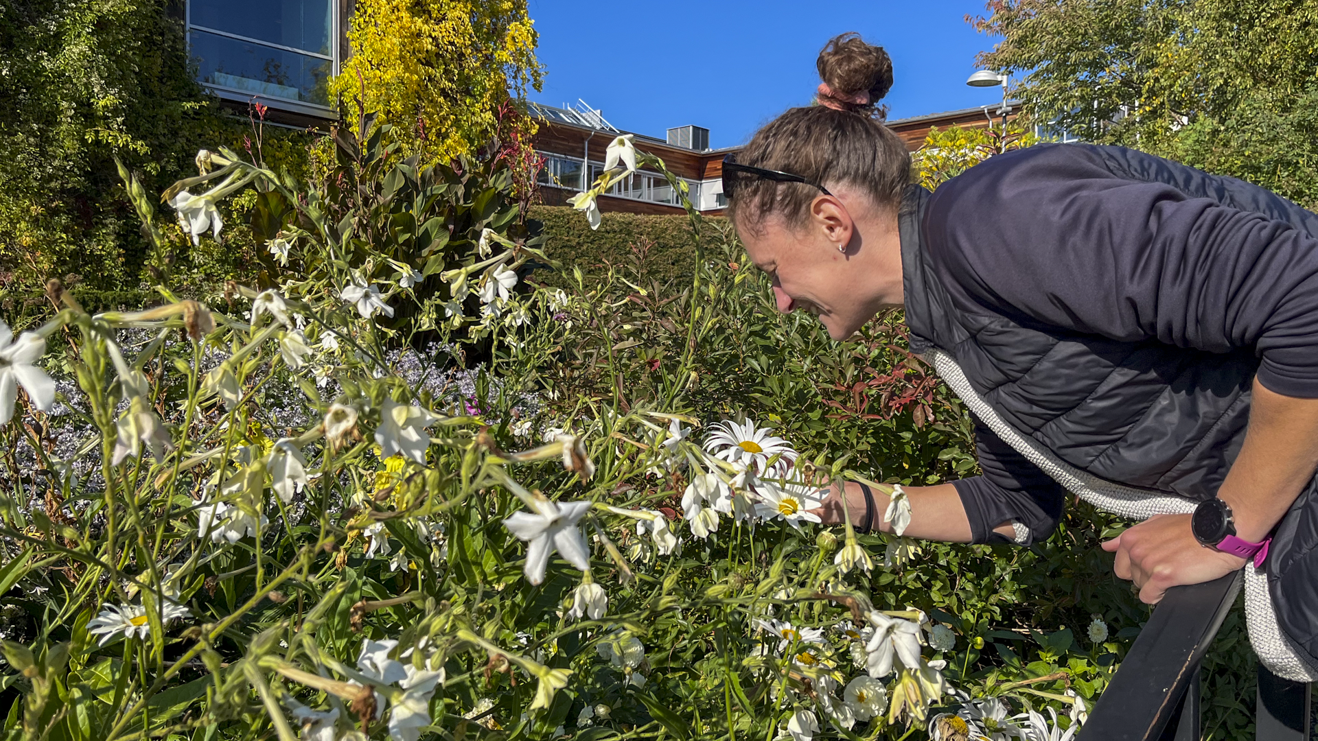 Francesca leans over some flowers and smells them