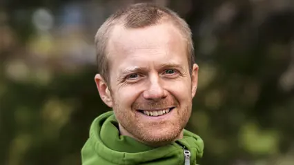 Porträtt av leende person i grön tröja utomhus.