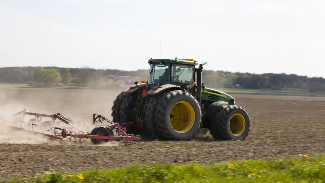 En traktor med harv kör på ett fält.