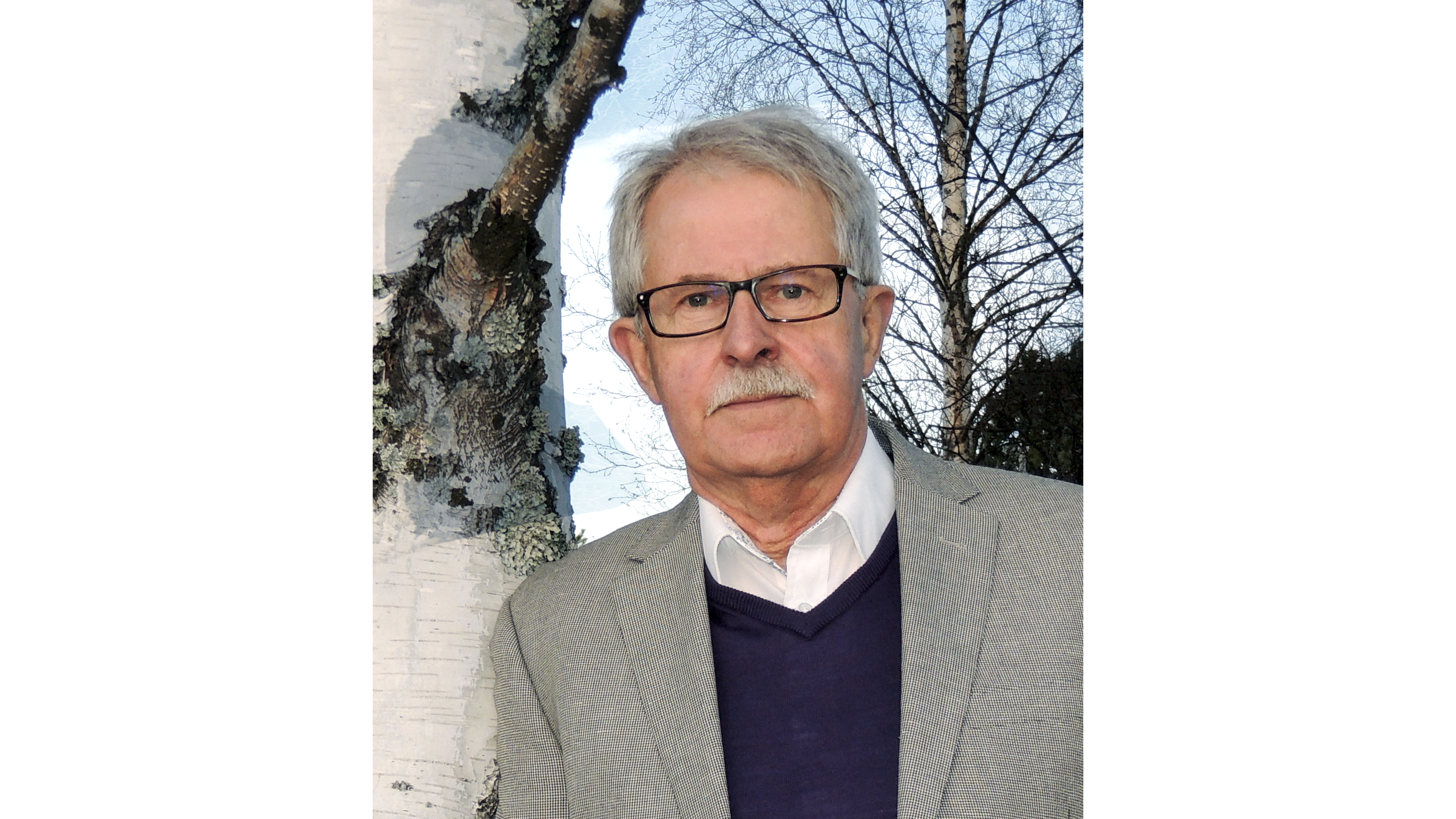 Man med grått kort hår, mustasch glasögon och grå kavaj. Foto