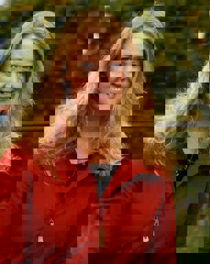 A woman with long, blond hair and a red jacket outdoors. Photo.