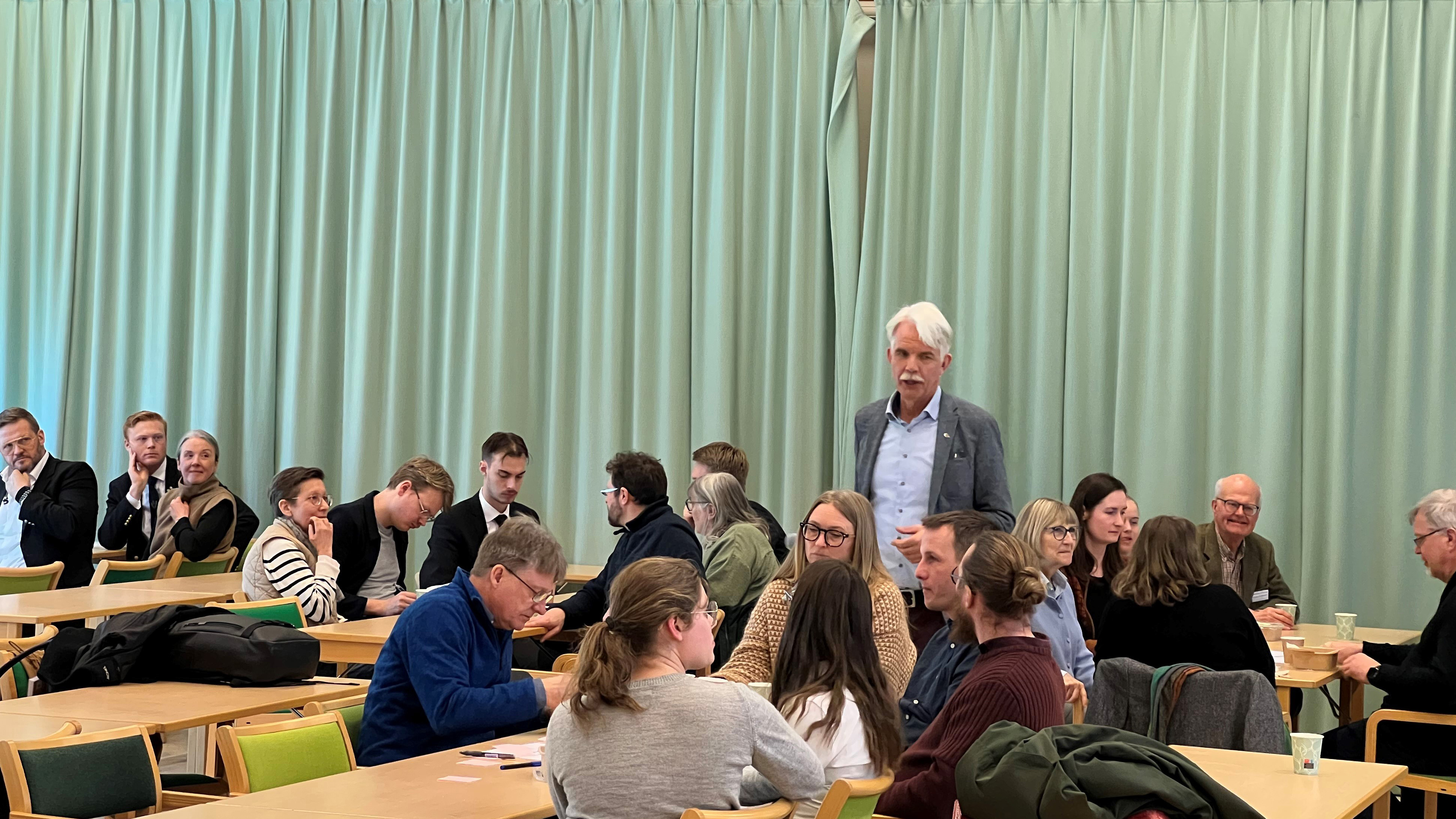 Personer sitter i grupper och lyssnar till en man