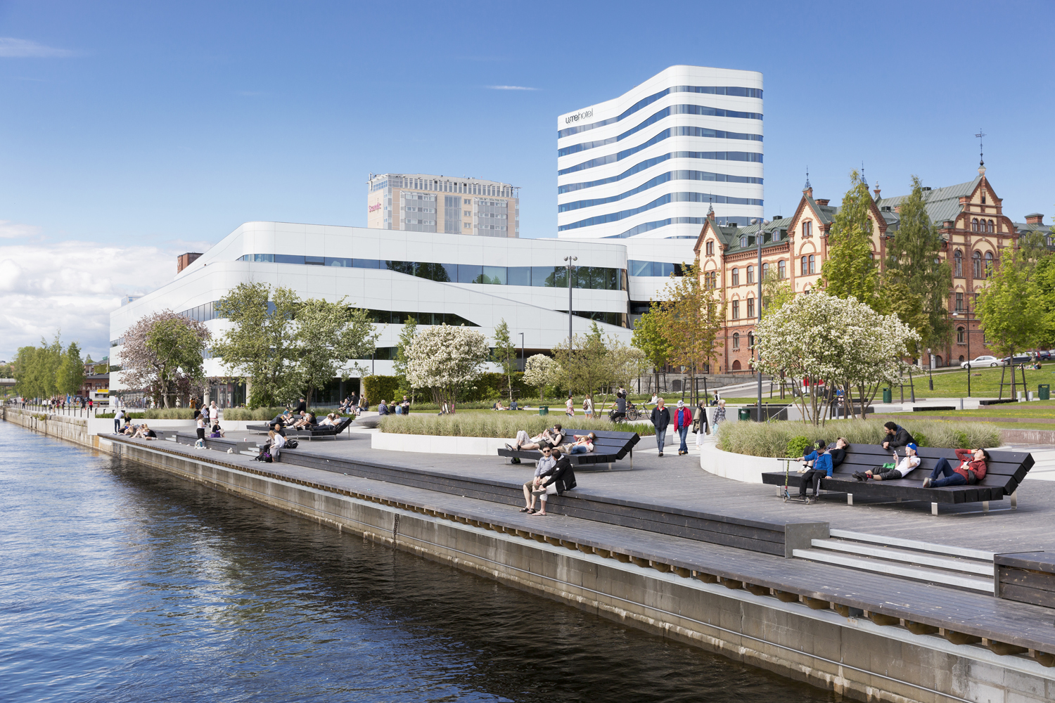 Promenadstråk vid vatten i en stad. I bakgrunden moderna och äldre byggnader. 