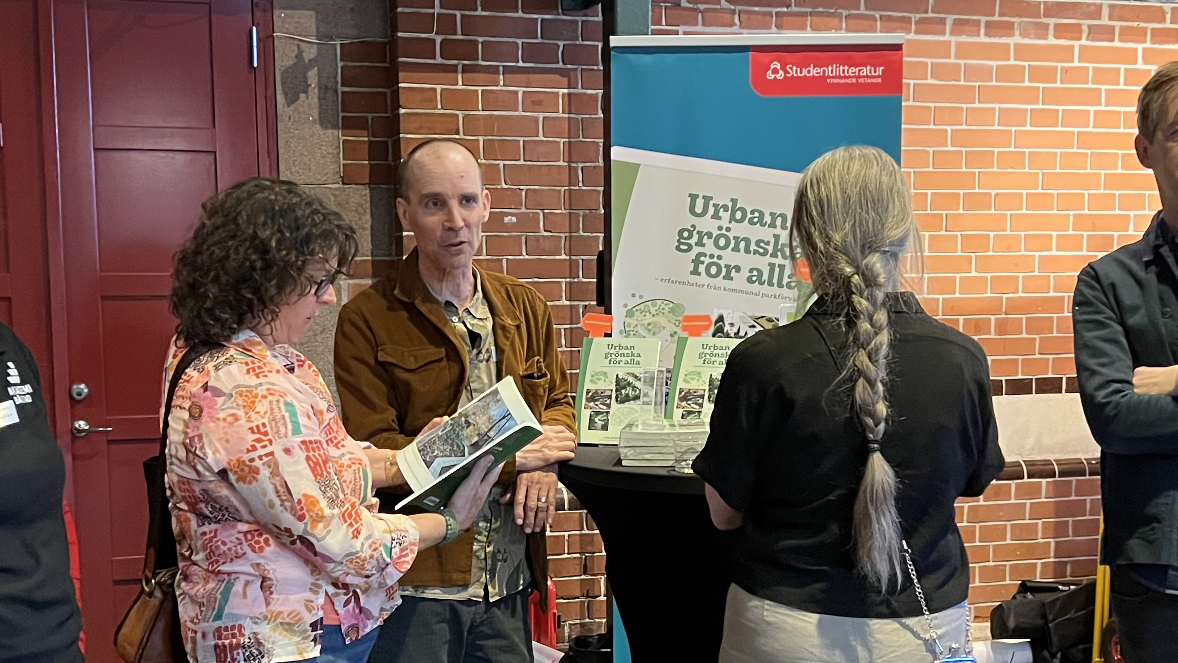 Lars står framför ett bokbord och pratar med några nyfikna personer.