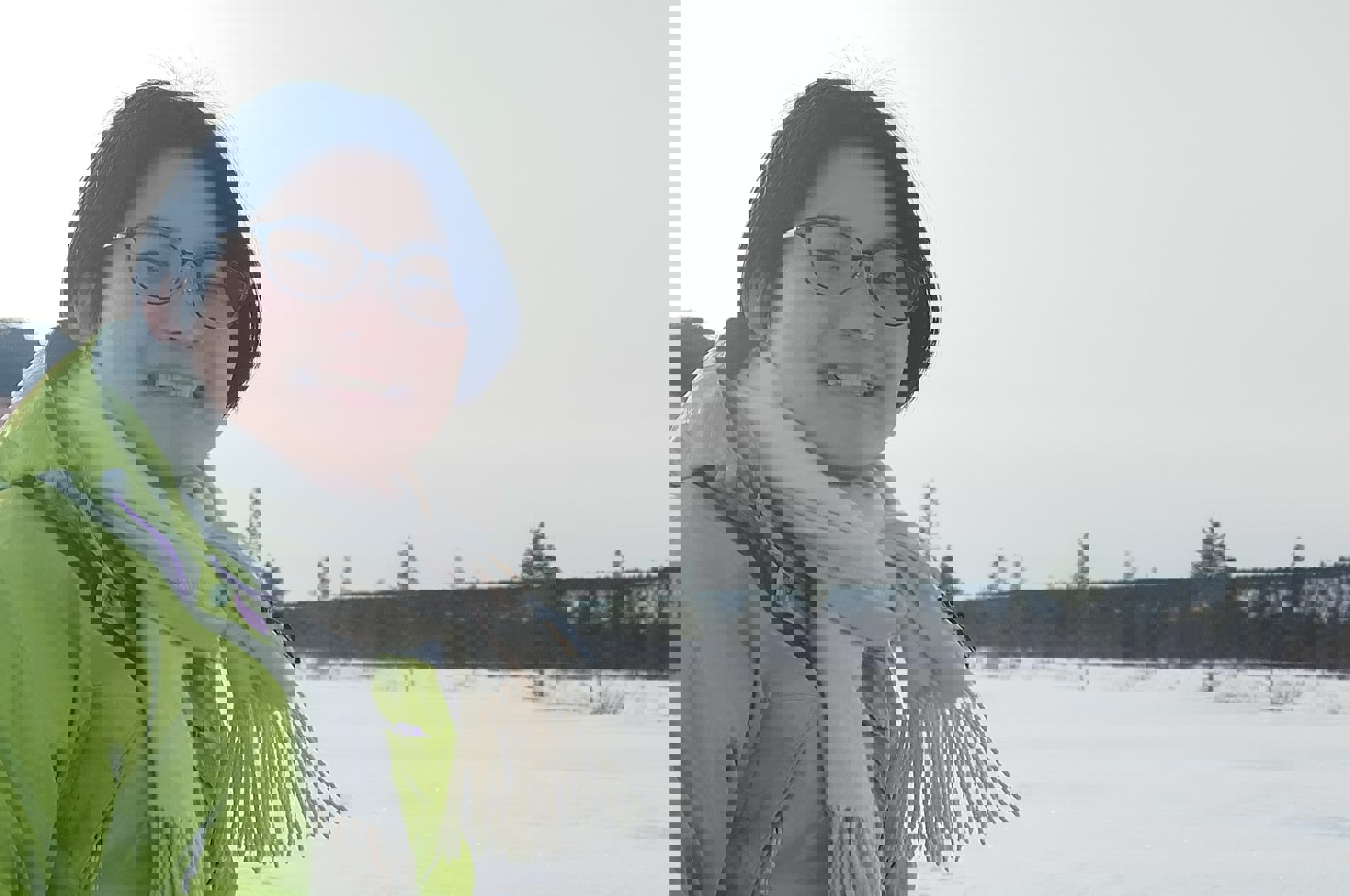 A smiling person in a green jacket and white scarf sitting outdoors in winter, with snow and other people in the background.