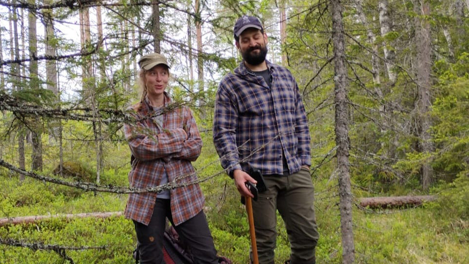 Two people standing in a green forest.