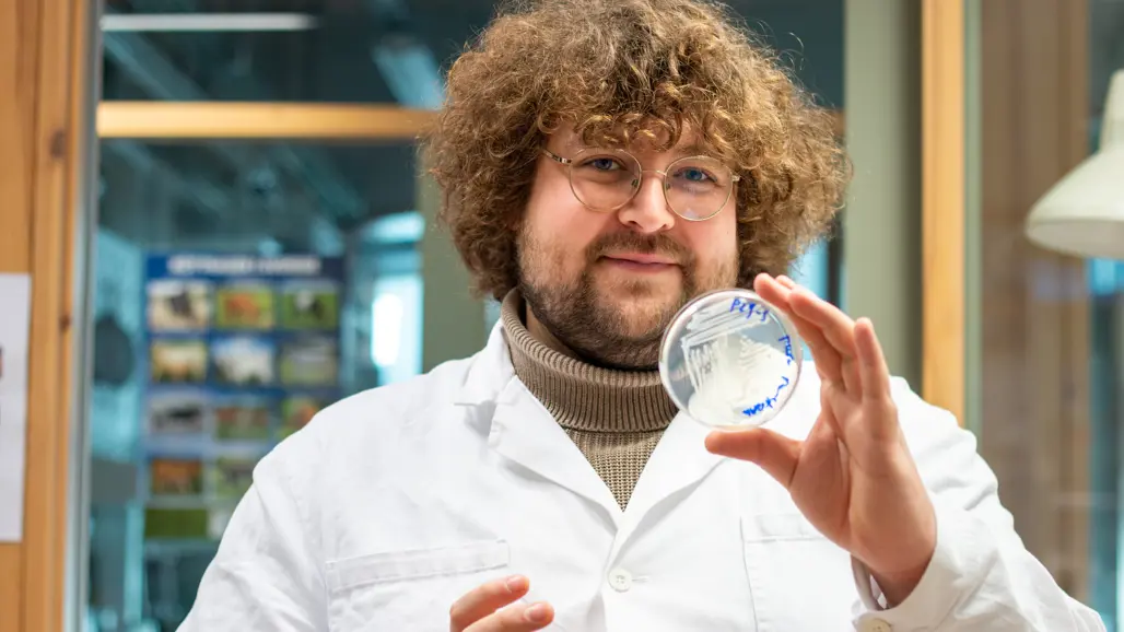 Portrait of a man (phd-student Lex Roelofs) in the laboratory dressed in lab gown holding a petri dish.