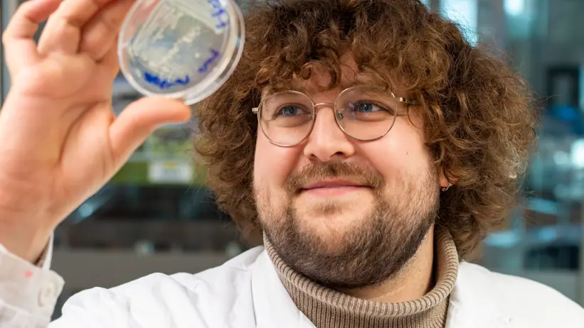 Portrait of a man (phd-student Lex Roelofs) in the laboratory dressed in lab gown holding a petri dish.