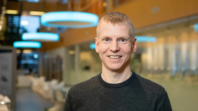 A man standing in a hallway smiling into the camera.