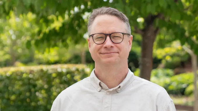 A person wearing glasses standing in a park looking into the camera.