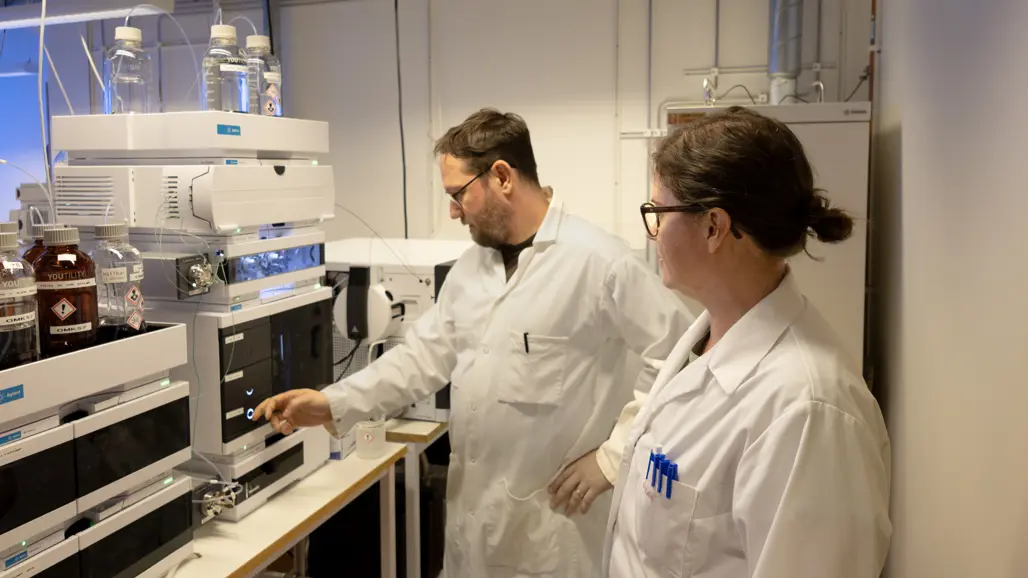 Two persons in front of a laboratory instrument. Photo.