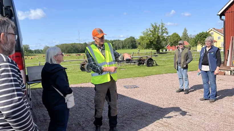 En person i varselväst förevisar en drönare på en gårdsplan, människor står runt omkring och tittar på. Foto.