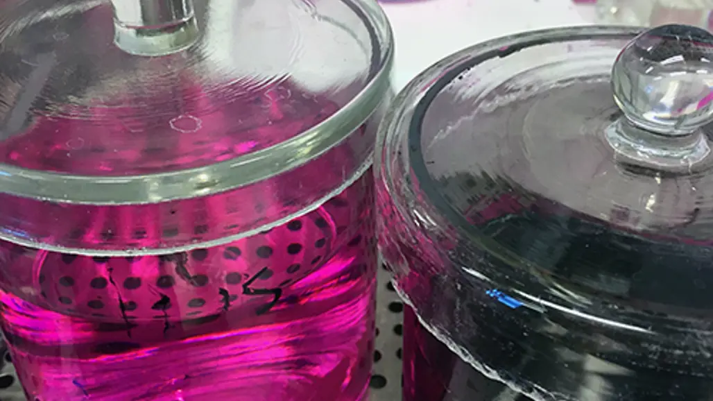 Two glass jars containing liquid. One contains pink liquid, the other clear liquid.