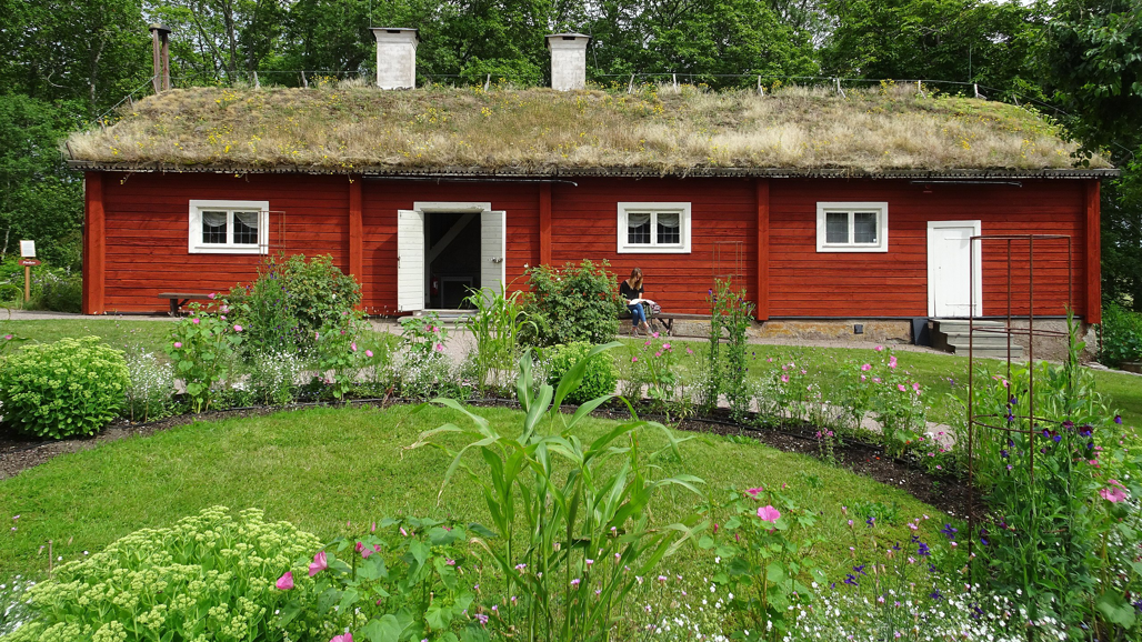A flowering garden in fornt of a red timber building with a grass ceiling.